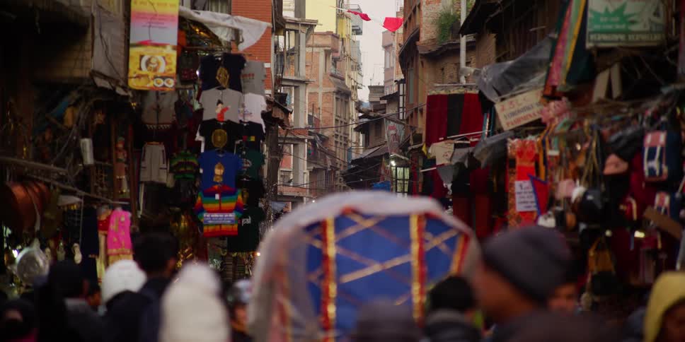 A rickshaw is surrounded by pedestrians as it makes its way down a street in a dense city in a developing country