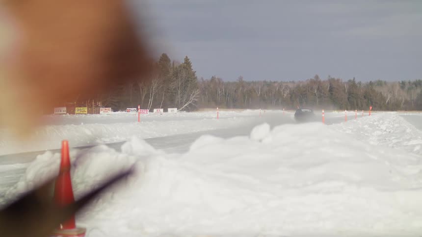 A black sports car speeding on an icy road with traffic cones
