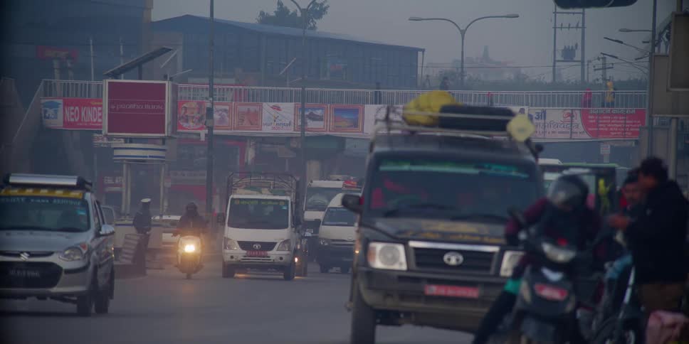 Traffic flows down foggy busy street as pedestrians cross bridge overhead