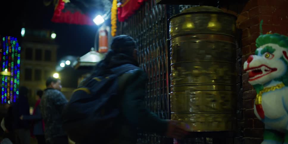 People in a foreign country walk down a street and stop and spin a wheel and then pray