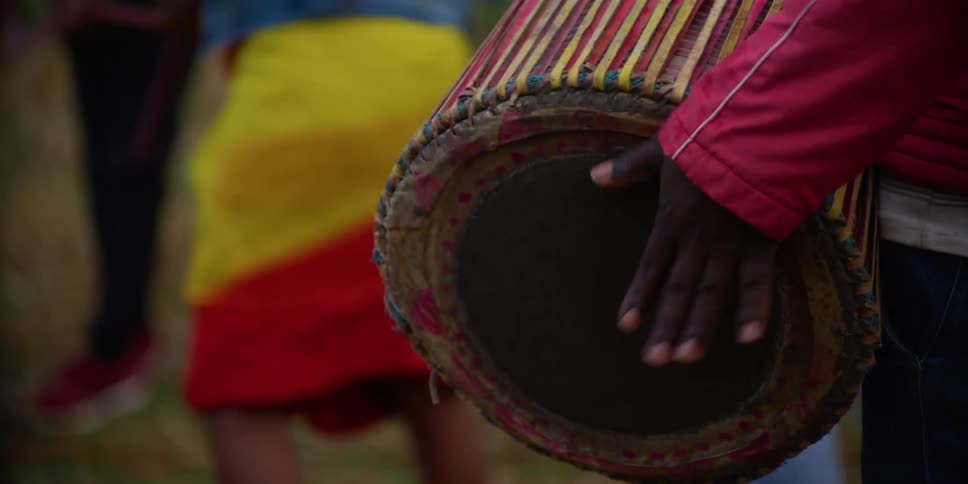 A person standing and playing a drum while people dance in the background
