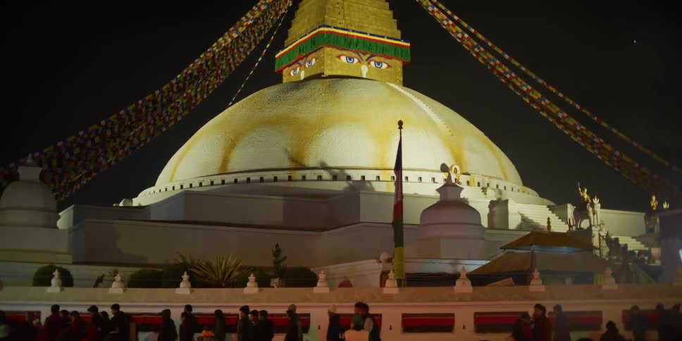 Crowd of people file past domed building decorated with eyes