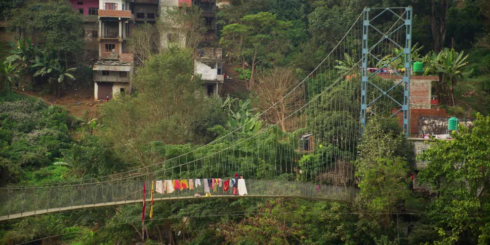 Woman hangs clothes to dry on a suspension bridge near the town on the mountains