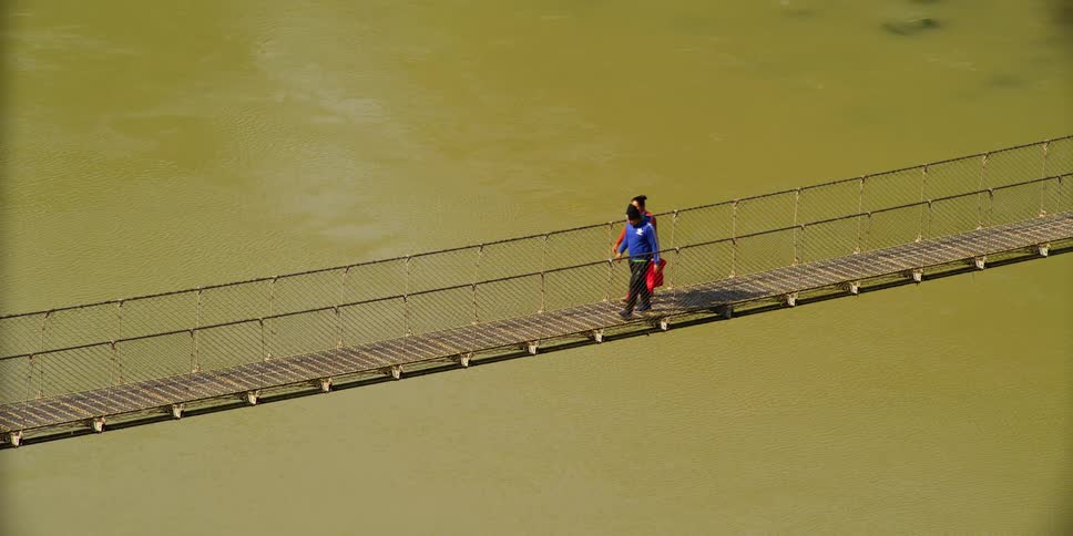 Two people are walking on a bridge over the river