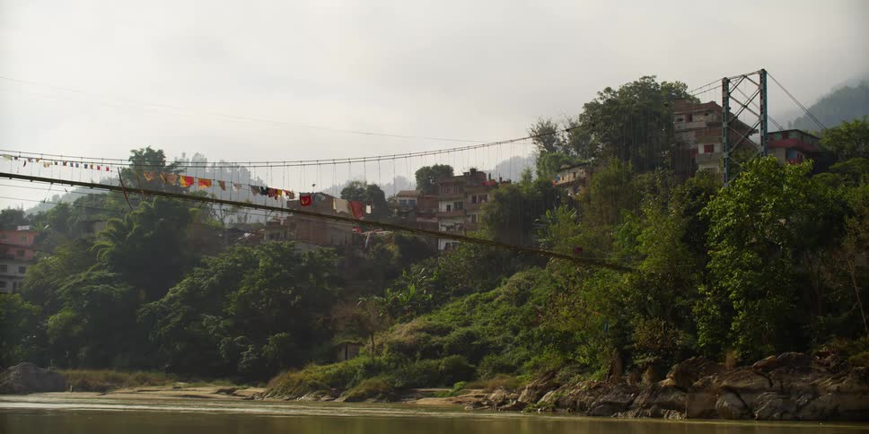 A narrow suspension bridge over a river outside of a rural town
