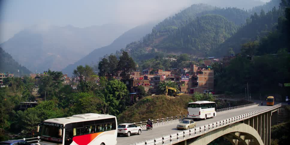 Many vehicles travel across a bridge near a small town in a mountainous region