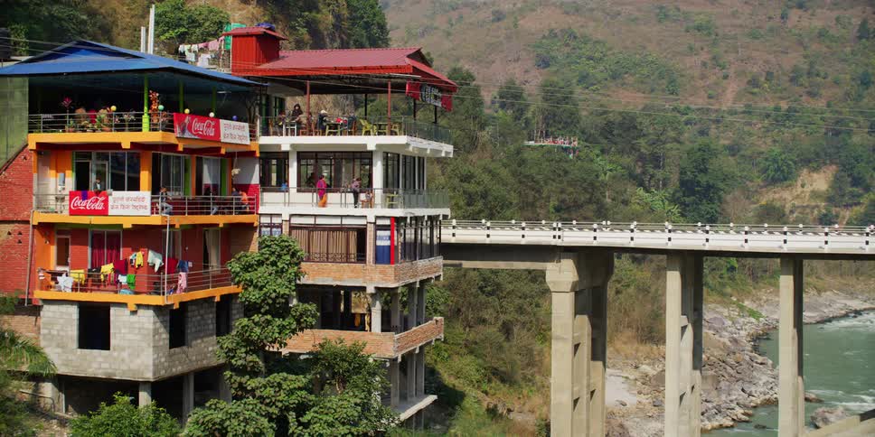 Car driving on a bridge over a river next to unfinished buildings on the slopes of a mountain