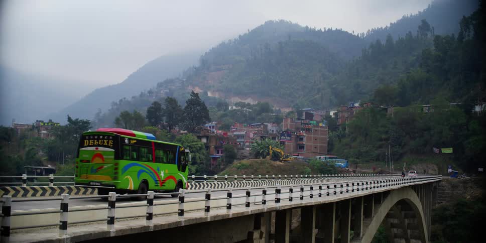 Bus crosses a bridge over a river next to a small town in the mountains
