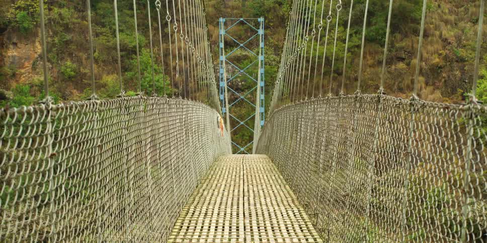 A simple suspension bridge leading to a hill covered in vegetation