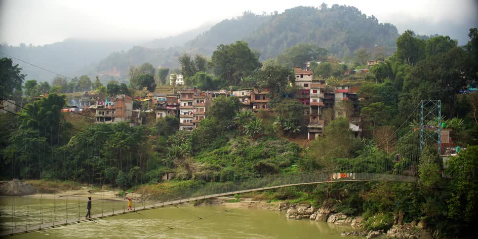Two people walk across a suspension bridge towards a neighborhood