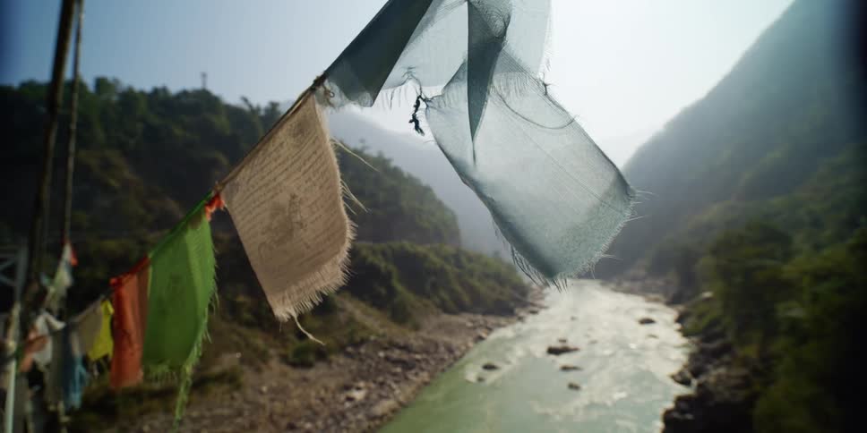 Tibetan prayer flags hanging over a river near the mountains