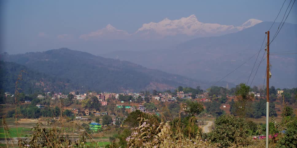Power lines lead over countryside to town nestled against fog covered mountain