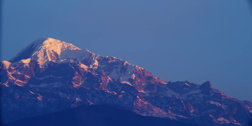 Snow covers summit of large mountain under clear blue sky