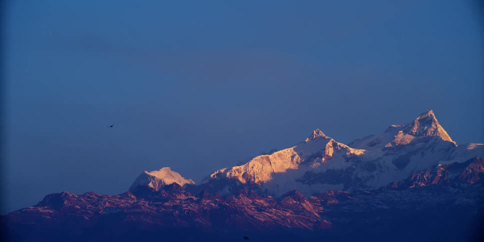 Birds flying in front of a snow covered peaks of a mountain range at sunset