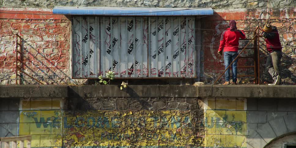 Two people stand on a ledge on a building and look at graffiti