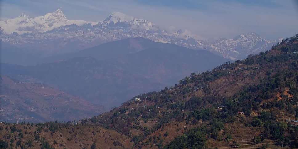 Houses on the slopes of a mountain near the snow covered peaks of a mountain range