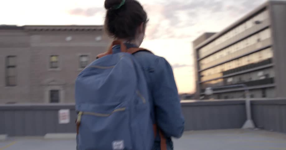 A woman wearing a backpack walks across the top of a parking ramp