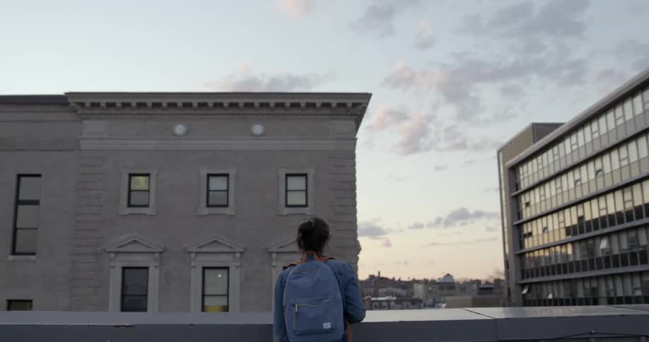 A young woman stands on the roof of a building looking out at a city