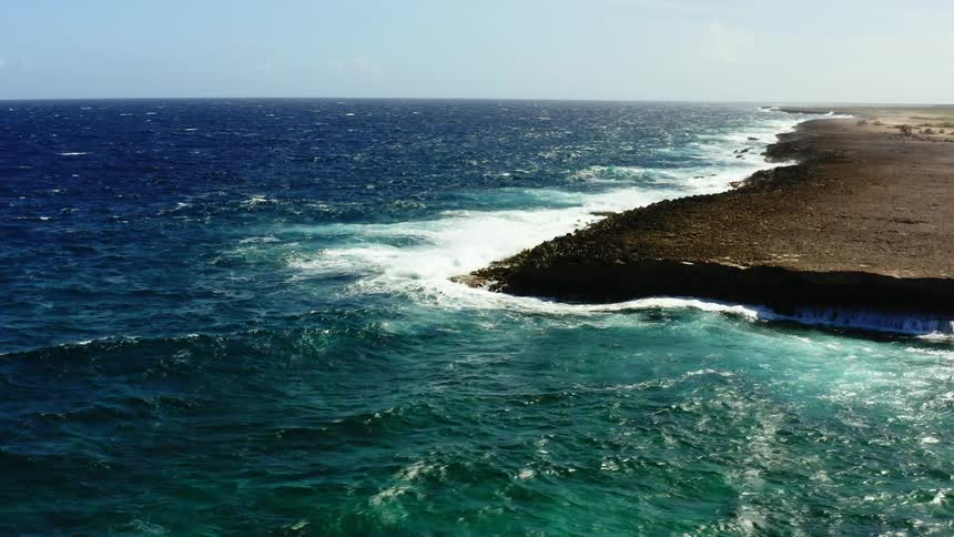 Ocean waves move swiftly and break against a raised and rocky shoreline