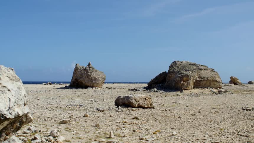 A flat coastline covered in both small stones and large boulders under a clear daytime sky