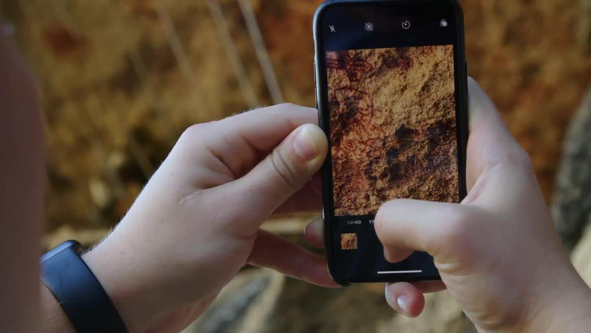 A person with a wristwatch holding a smartphone and taking a picture of cave art