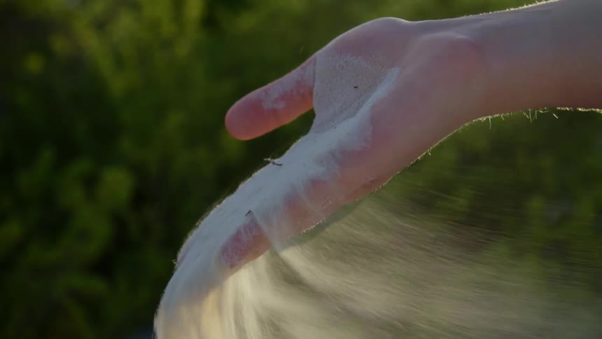 A person opens their hands to allow sand to pour out and be blown away by the wind