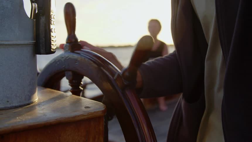 A man steering a boat as a lady sitting watches him steer