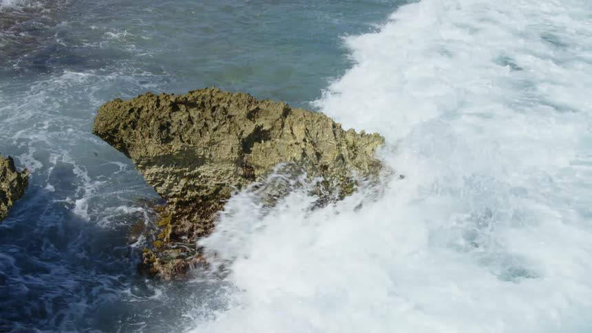 An ocean wave crashing into a rock on a beach