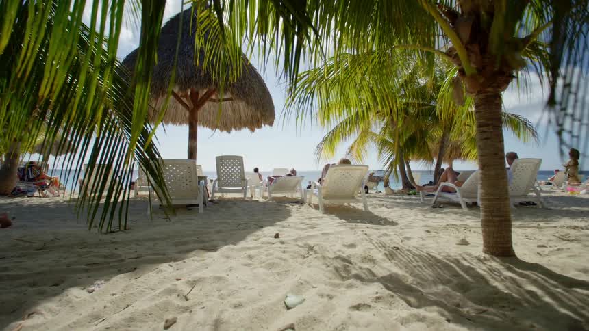 People relax on beach chairs and under straw huts at a beach resort