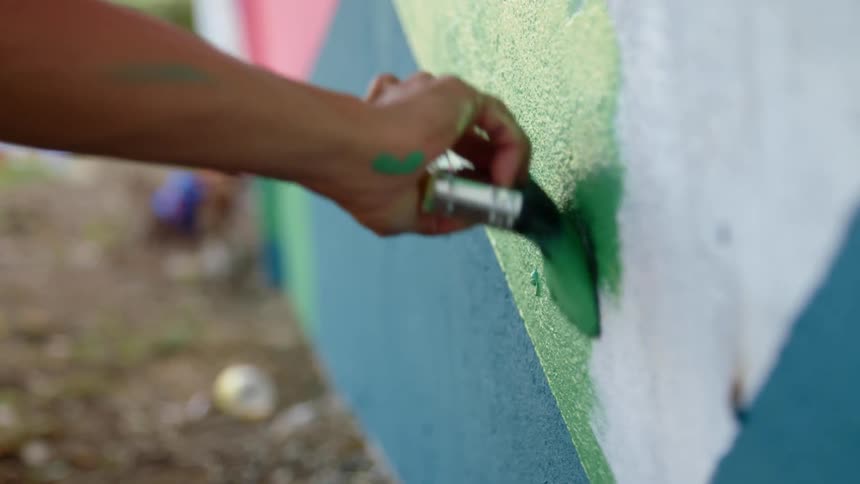 A person paints a wall with bright colors using a brush outdoors