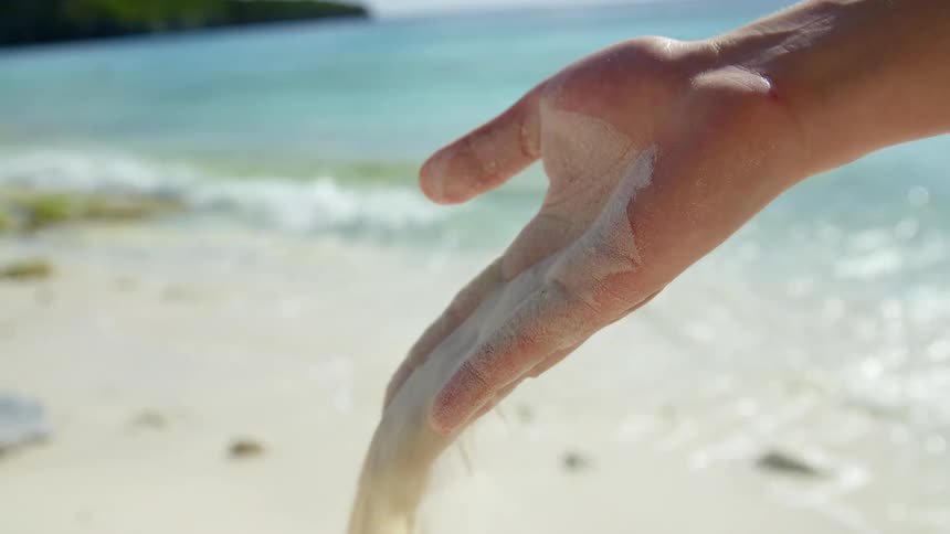 A womans is holding sand at the beach