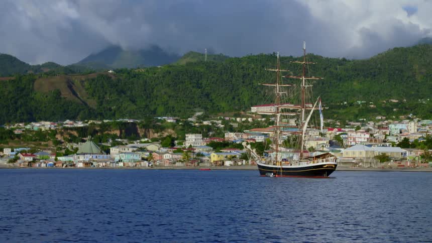 A ship floating off the coast of a town on a summer day