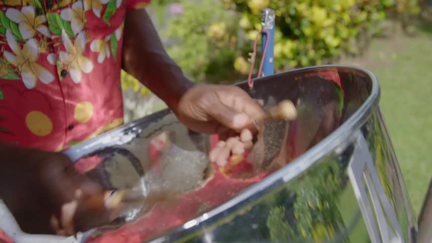A drummer playing a metal drum in a tropical button up shirt