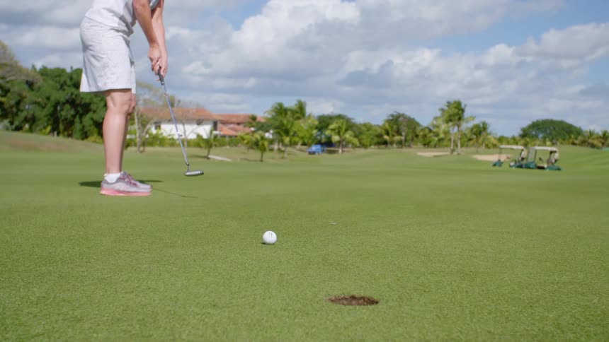 A golfer sinks a shot on the green and celebrates by lifting his arm and tilting backwards
