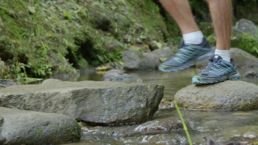 A person with sneakers walking on stones over a stream
