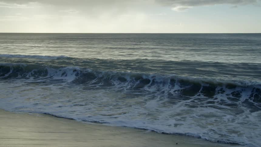 Ocean waves break against the beach at dusk