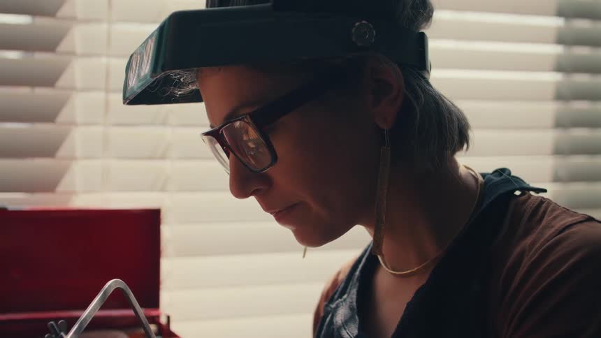 Young woman wearing glasses prepares to make a cut with a saw in her workshop