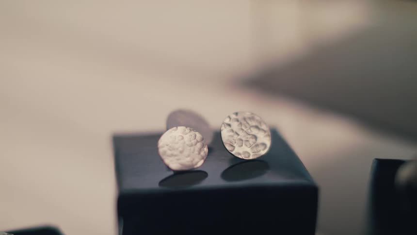 A pair of silver hammered earrings sit on a glossy black box near other jewelry in a display