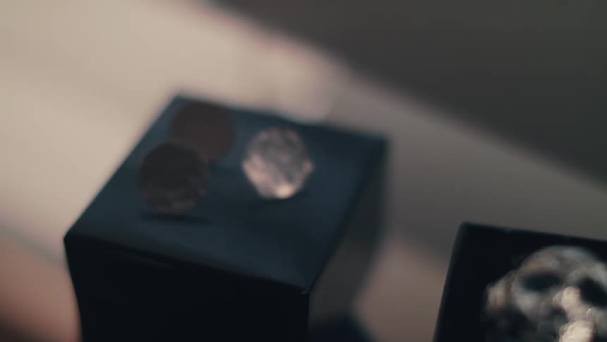 Metal jewelry in shapes including a skull and hammered discs sit on black boxes on a ledge in a shop