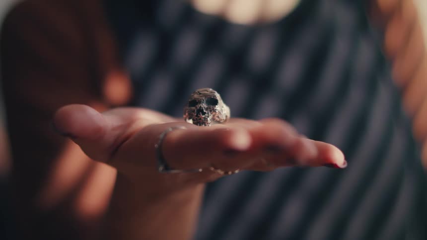 A ring shaped light a skull rests on the open palm of a woman wearing dark fingernail polish