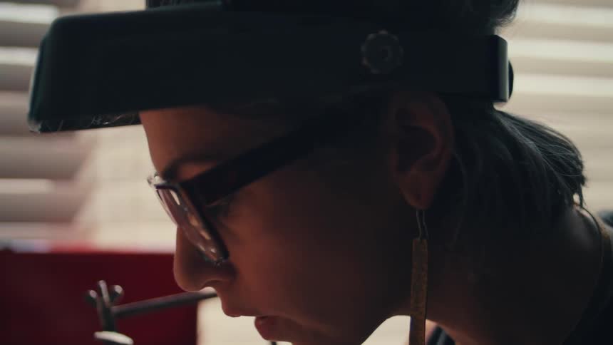 A woman with glasses earrings and goggles on her head using a saw