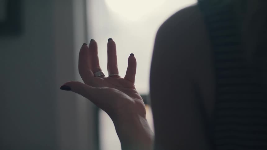 A woman standing indoors near a window slowly twirls her hand