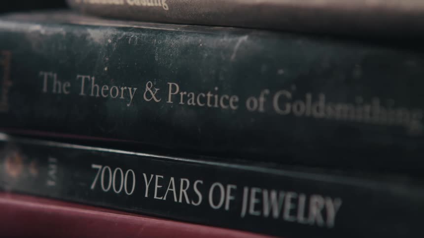 Books on jewelry and goldsmithing are stacked vertically in a room