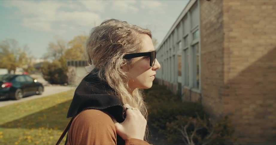 A woman walks in front of a building holding something on her shoulder