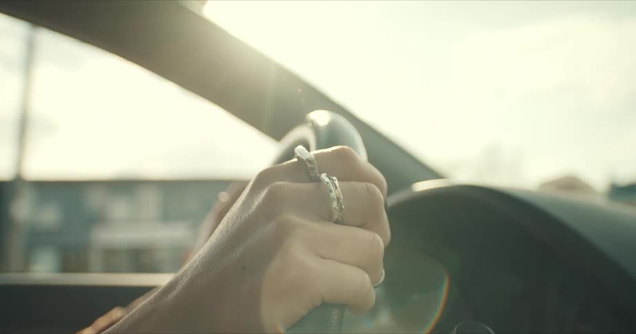 Woman with rings on her fingers drives a car at sunset