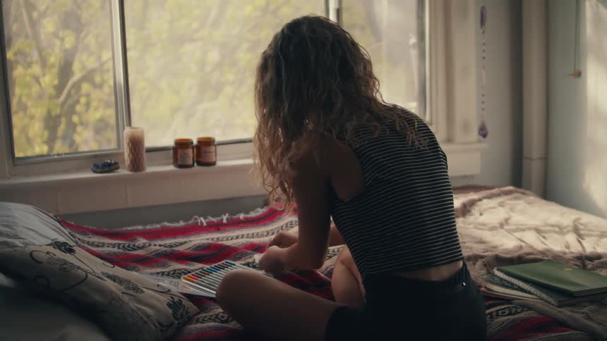 A woman sits on a bed near a window