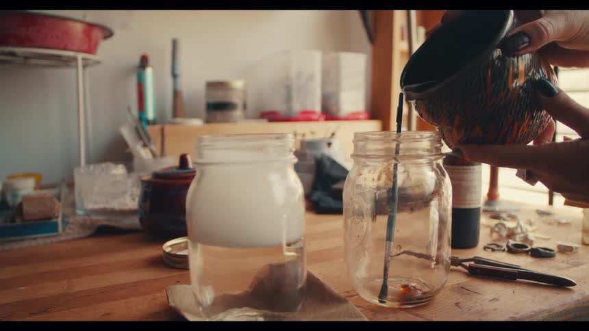Woman at workbench mixes liquids with paintbrush
