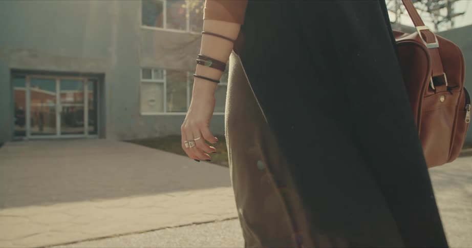 Woman wearing cloak and carrying bag walks toward building entrance