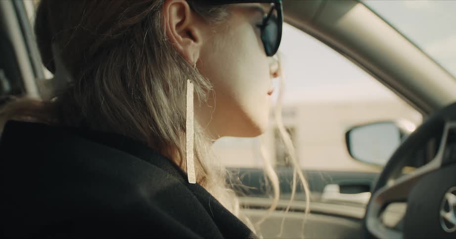 Side view of a blonde woman with glasses and earrings driving a car