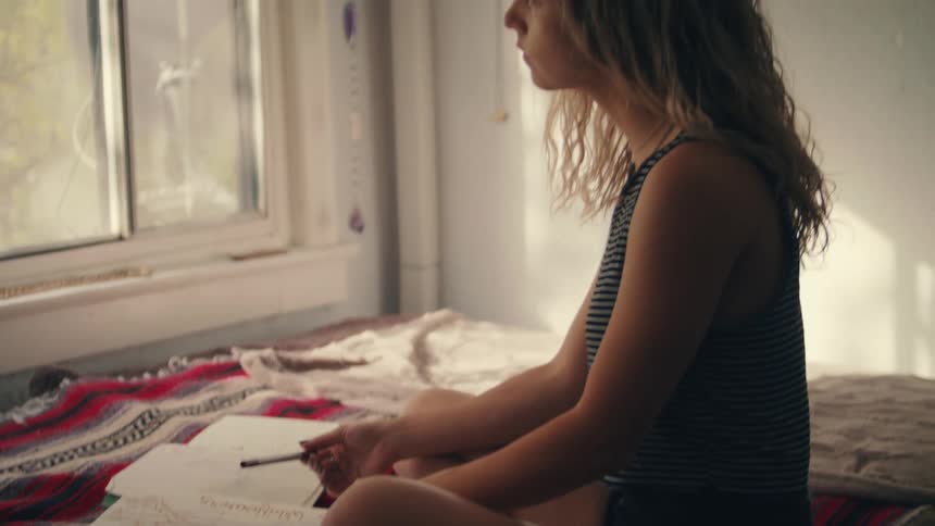 Young woman sitting on the bed at home looks out the window